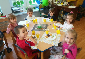 Dzieci przy stoliku degustują ciasteczka w wielkanocnych kształtach.